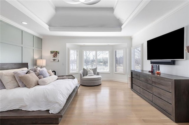 bedroom with light wood-style flooring, a raised ceiling, baseboards, and ornamental molding