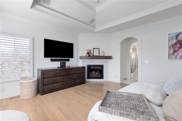 bedroom featuring ornamental molding, wood finished floors, arched walkways, a fireplace, and a raised ceiling