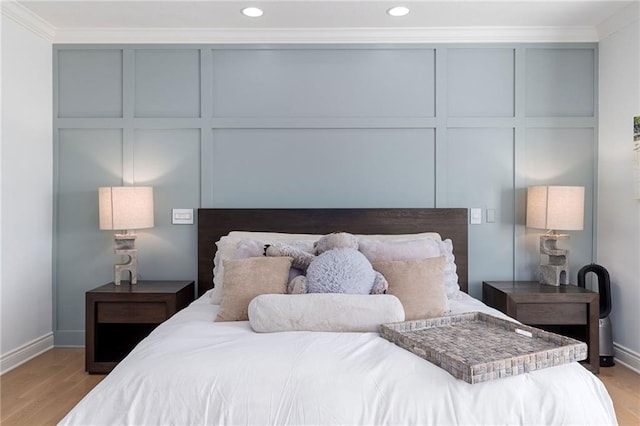 bedroom featuring recessed lighting, light wood-type flooring, crown molding, and a decorative wall