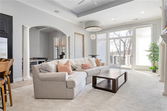 living room featuring baseboards, decorative columns, arched walkways, crown molding, and light colored carpet