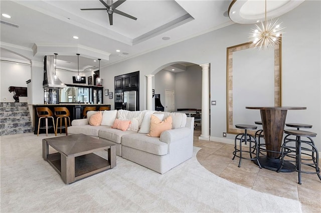 living room featuring visible vents, a ceiling fan, a tray ceiling, arched walkways, and ornate columns