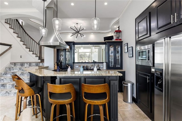 kitchen featuring a kitchen breakfast bar, a kitchen island, appliances with stainless steel finishes, light stone countertops, and dark cabinets