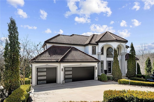 mediterranean / spanish house with a garage, a tile roof, concrete driveway, and stucco siding