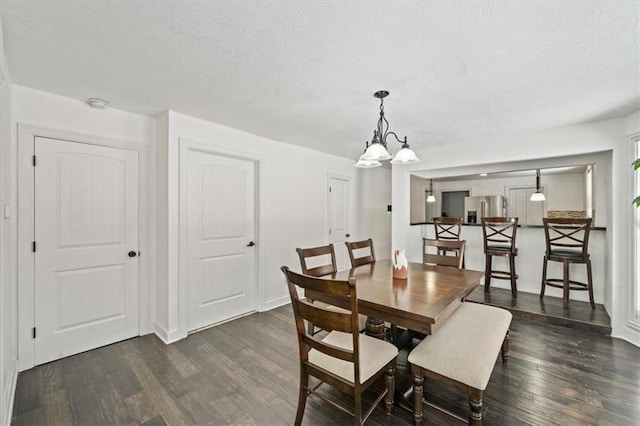 dining area with dark wood-type flooring, a notable chandelier, a textured ceiling, and baseboards