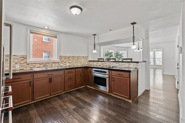 kitchen with dark countertops, a sink, stainless steel oven, and pendant lighting