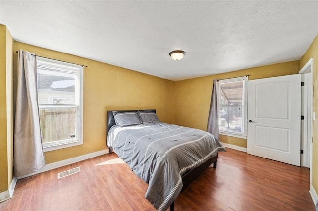 bedroom featuring dark wood-style floors, visible vents, a textured ceiling, and baseboards