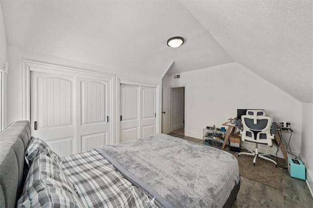 bedroom featuring baseboards, visible vents, dark wood-type flooring, vaulted ceiling, and multiple closets