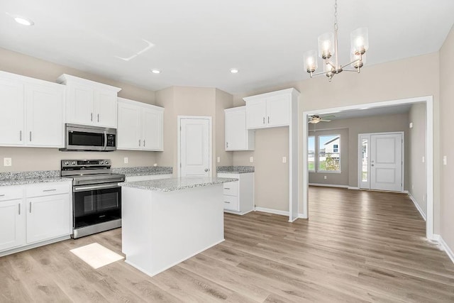 kitchen featuring appliances with stainless steel finishes, white cabinets, light stone countertops, and a center island