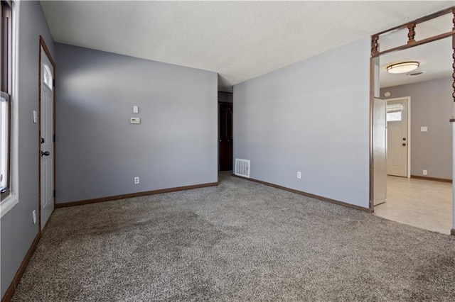 empty room featuring light colored carpet, visible vents, baseboards, and a textured ceiling