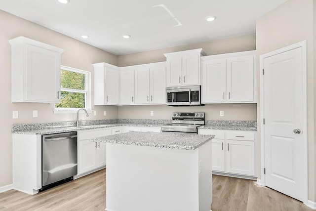 kitchen featuring appliances with stainless steel finishes, light stone counters, a kitchen island, sink, and white cabinetry