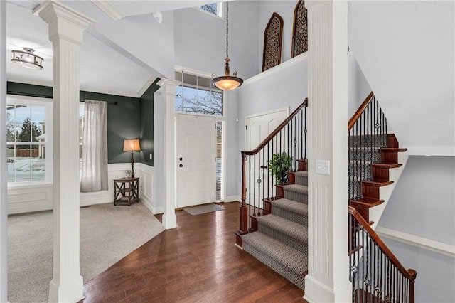 foyer with stairway, wainscoting, ornate columns, dark wood finished floors, and crown molding