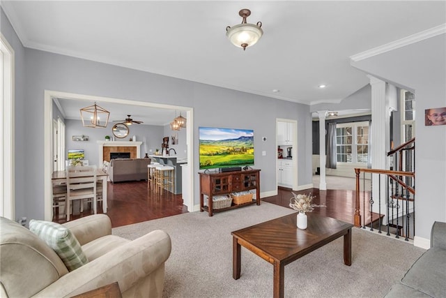 carpeted living area featuring baseboards, crown molding, a tiled fireplace, and decorative columns