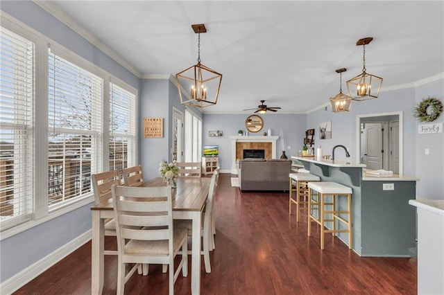 dining space with baseboards, dark wood-style floors, crown molding, a fireplace, and ceiling fan with notable chandelier