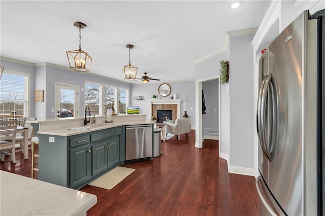 kitchen with a tile fireplace, ceiling fan with notable chandelier, a sink, light countertops, and appliances with stainless steel finishes