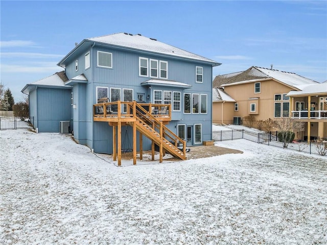 snow covered back of property with stairs, a fenced backyard, a wooden deck, and central air condition unit