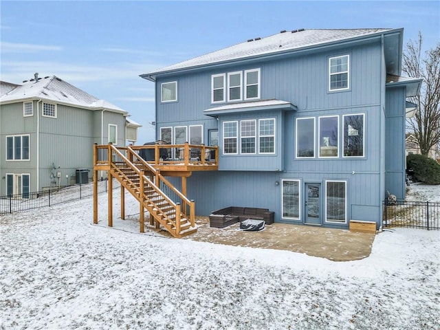 snow covered back of property with a deck, central air condition unit, fence, stairs, and a patio area