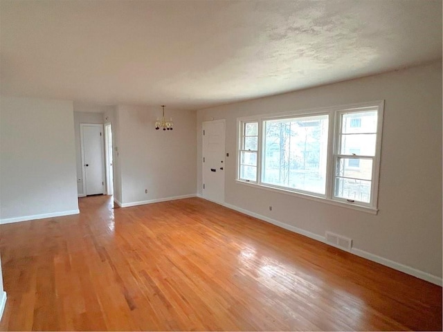 empty room with light wood-type flooring and a notable chandelier