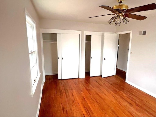 unfurnished bedroom with hardwood / wood-style flooring, multiple closets, and ceiling fan