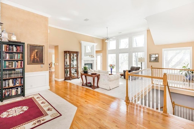 interior space featuring wainscoting, wood finished floors, crown molding, an upstairs landing, and a fireplace