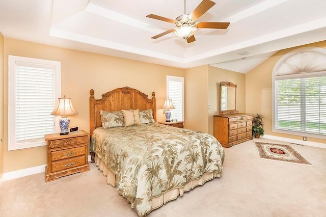 bedroom featuring light carpet, baseboards, a raised ceiling, and a ceiling fan