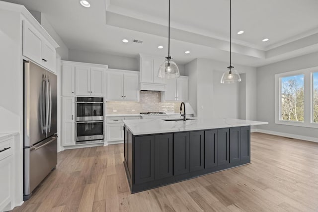 kitchen featuring a tray ceiling, white cabinetry, stainless steel appliances, and a kitchen island with sink