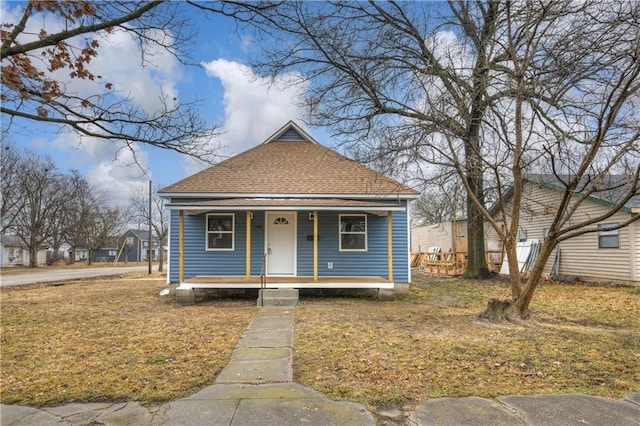 bungalow-style home with covered porch, a shingled roof, and a front lawn