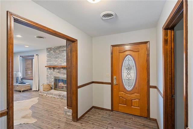 entryway featuring baseboards, a fireplace, visible vents, and wood finished floors