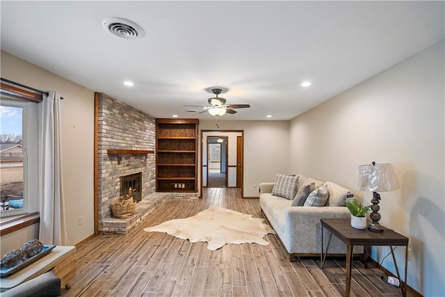 living room featuring recessed lighting, visible vents, a ceiling fan, a brick fireplace, and light wood-type flooring