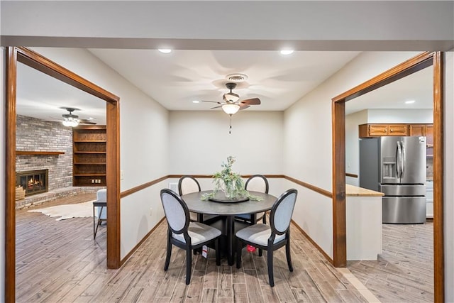 dining area featuring light wood-style flooring, a fireplace, and a ceiling fan