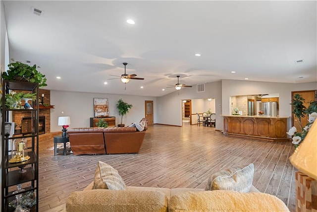 living room featuring lofted ceiling, visible vents, a fireplace, and wood finished floors