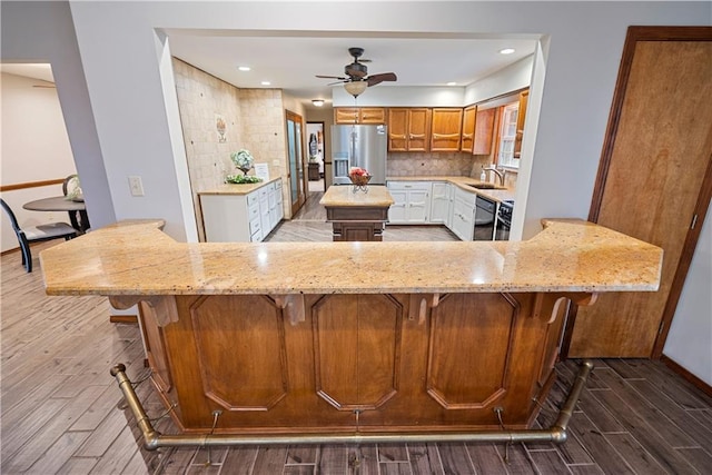 kitchen featuring stainless steel refrigerator with ice dispenser, white cabinets, a peninsula, and light stone countertops