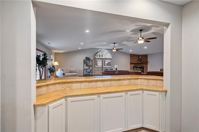 kitchen featuring open floor plan, a brick fireplace, lofted ceiling, and white cabinetry