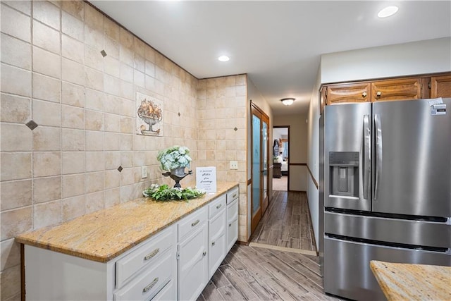 kitchen with stainless steel fridge, white cabinets, light wood-style flooring, light stone countertops, and tile walls