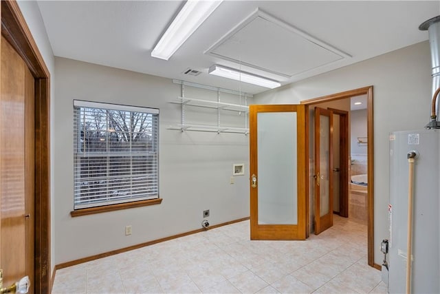 spare room with visible vents, gas water heater, attic access, and baseboards