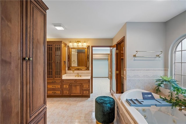 bathroom with tile walls, vanity, wainscoting, tile patterned floors, and a whirlpool tub