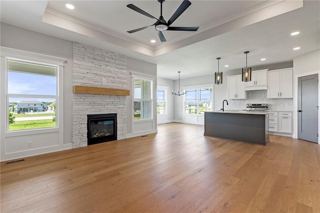 17151 W 168th Pl, Olathe, KS 66062 - unfurnished living room featuring a ceiling fan, light wood-style flooring, a raised ceiling, recessed lighting, and a stone fireplace