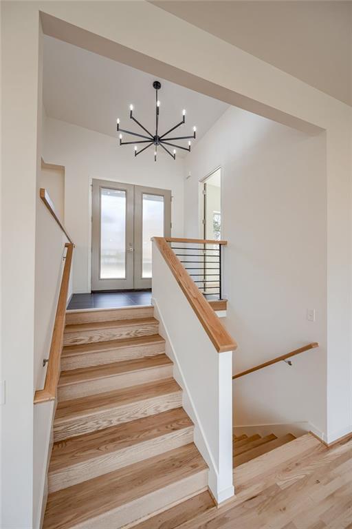 stairs with french doors, wood finished floors, and a chandelier