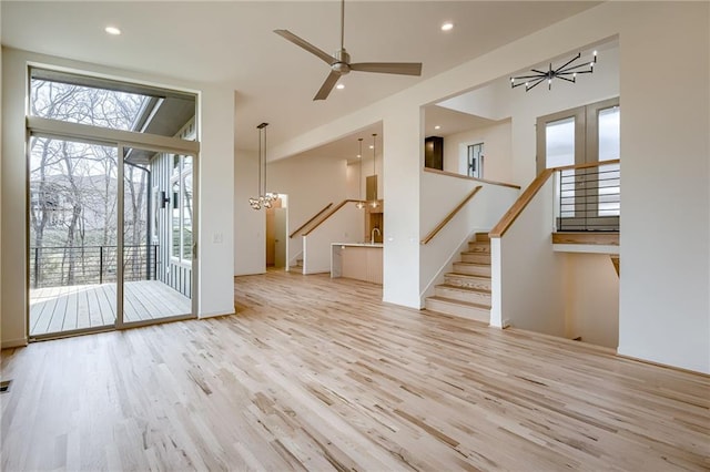 unfurnished living room with stairs, ceiling fan with notable chandelier, wood finished floors, and recessed lighting