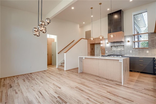 kitchen with decorative backsplash, light wood-style flooring, light countertops, and wall chimney range hood