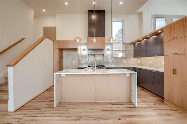 kitchen with modern cabinets, light wood-style flooring, an island with sink, backsplash, and light stone countertops