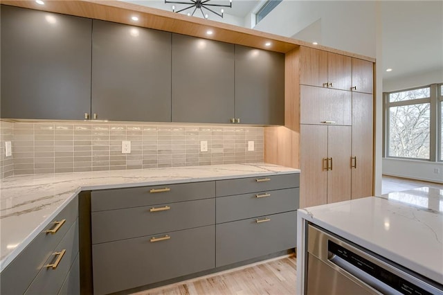 kitchen featuring stainless steel dishwasher, light stone counters, tasteful backsplash, and gray cabinetry