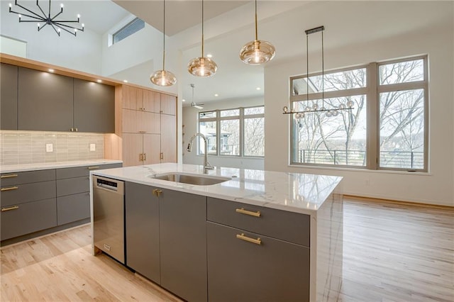 kitchen featuring gray cabinets, a sink, plenty of natural light, stainless steel dishwasher, and light wood-style floors