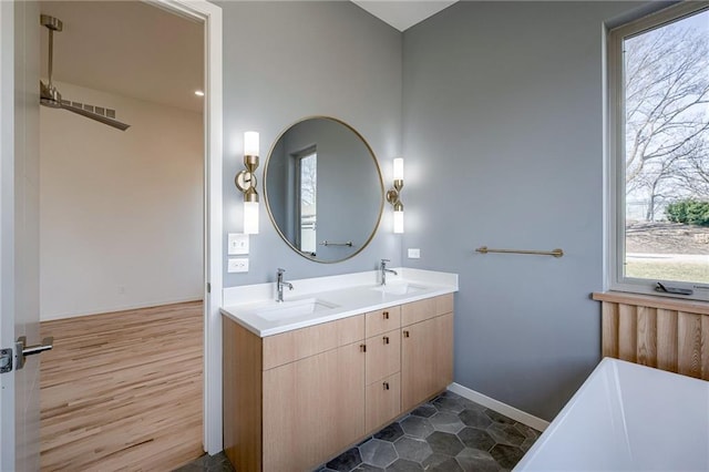 full bathroom with double vanity, a bathing tub, baseboards, and a sink