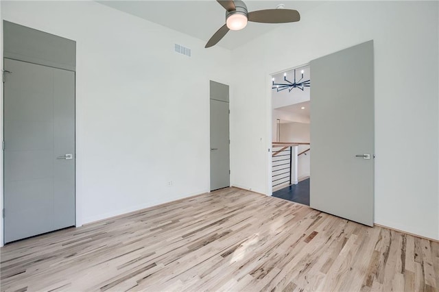 unfurnished bedroom featuring ceiling fan with notable chandelier, wood finished floors, and visible vents