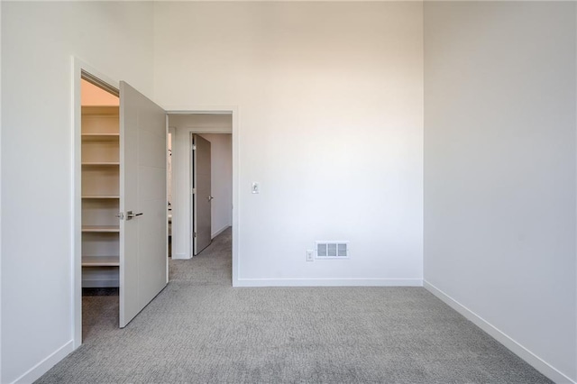 unfurnished bedroom featuring visible vents, light carpet, baseboards, and a walk in closet