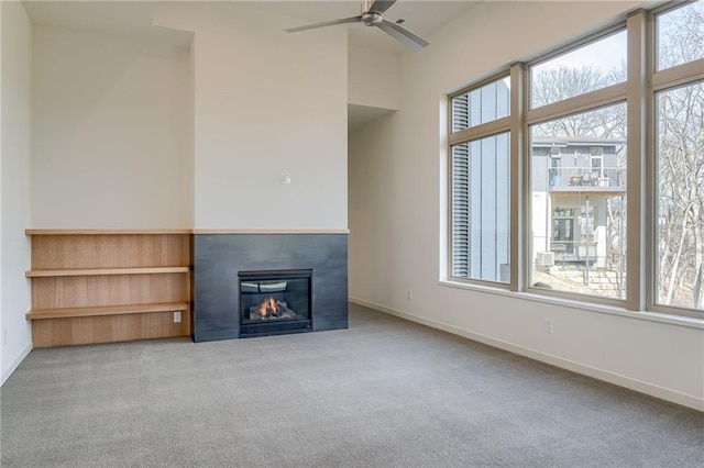 unfurnished living room featuring a glass covered fireplace, a ceiling fan, baseboards, and carpet floors