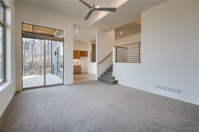 unfurnished living room with visible vents, baseboards, stairs, carpet flooring, and a ceiling fan