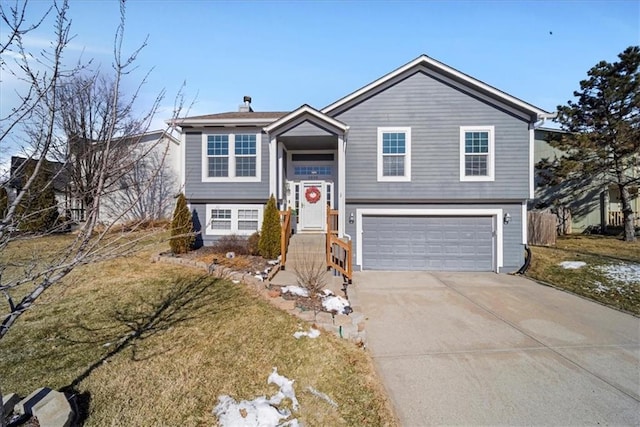 raised ranch featuring concrete driveway, an attached garage, and a front yard