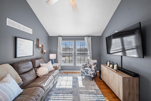 living room featuring lofted ceiling, light wood-type flooring, ceiling fan, and a textured ceiling