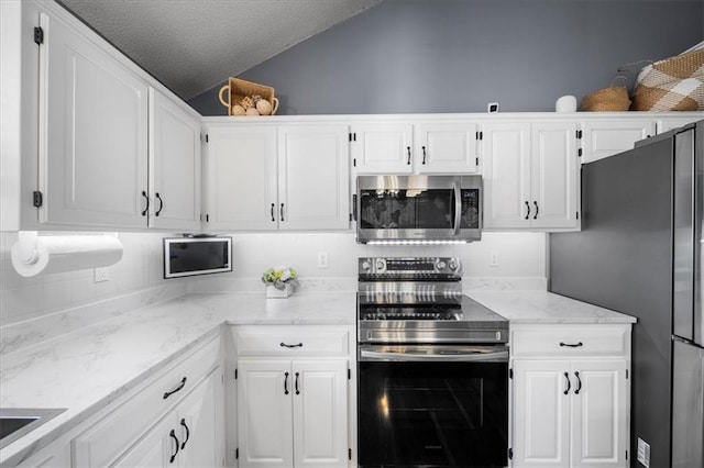 kitchen featuring lofted ceiling, appliances with stainless steel finishes, light stone countertops, a textured ceiling, and white cabinetry